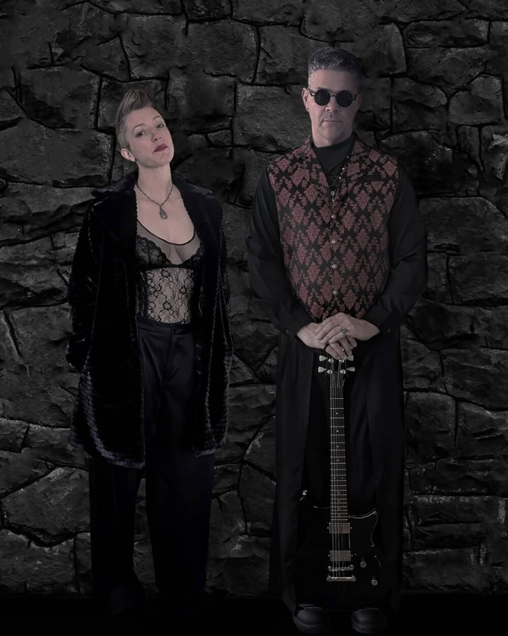Sister Medusa, the duo posing in front of a dark stone wall